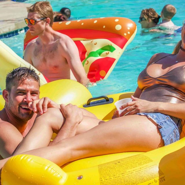 Couple floats in a pool on a rubber duck and pizza float