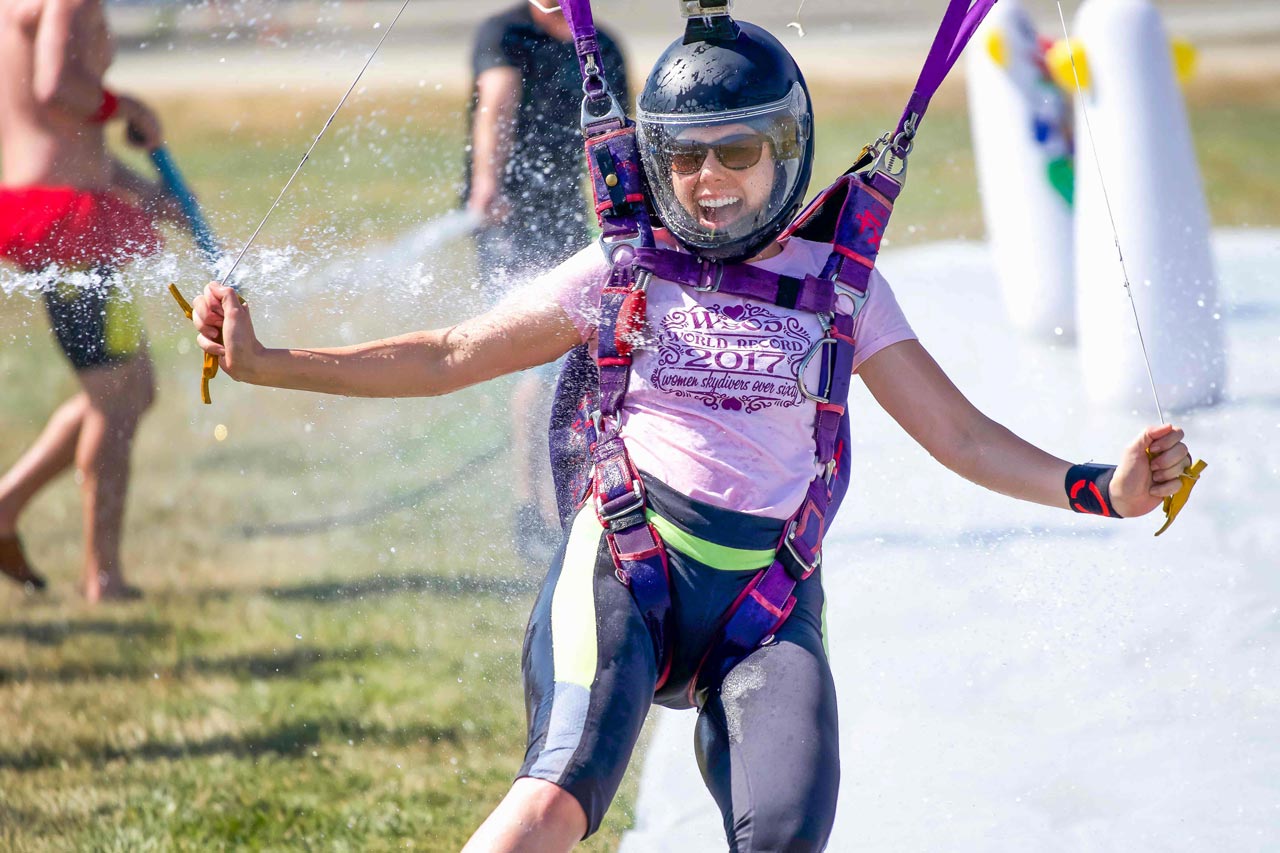 Female professional skydiver sliding through water on feet while landing parachute