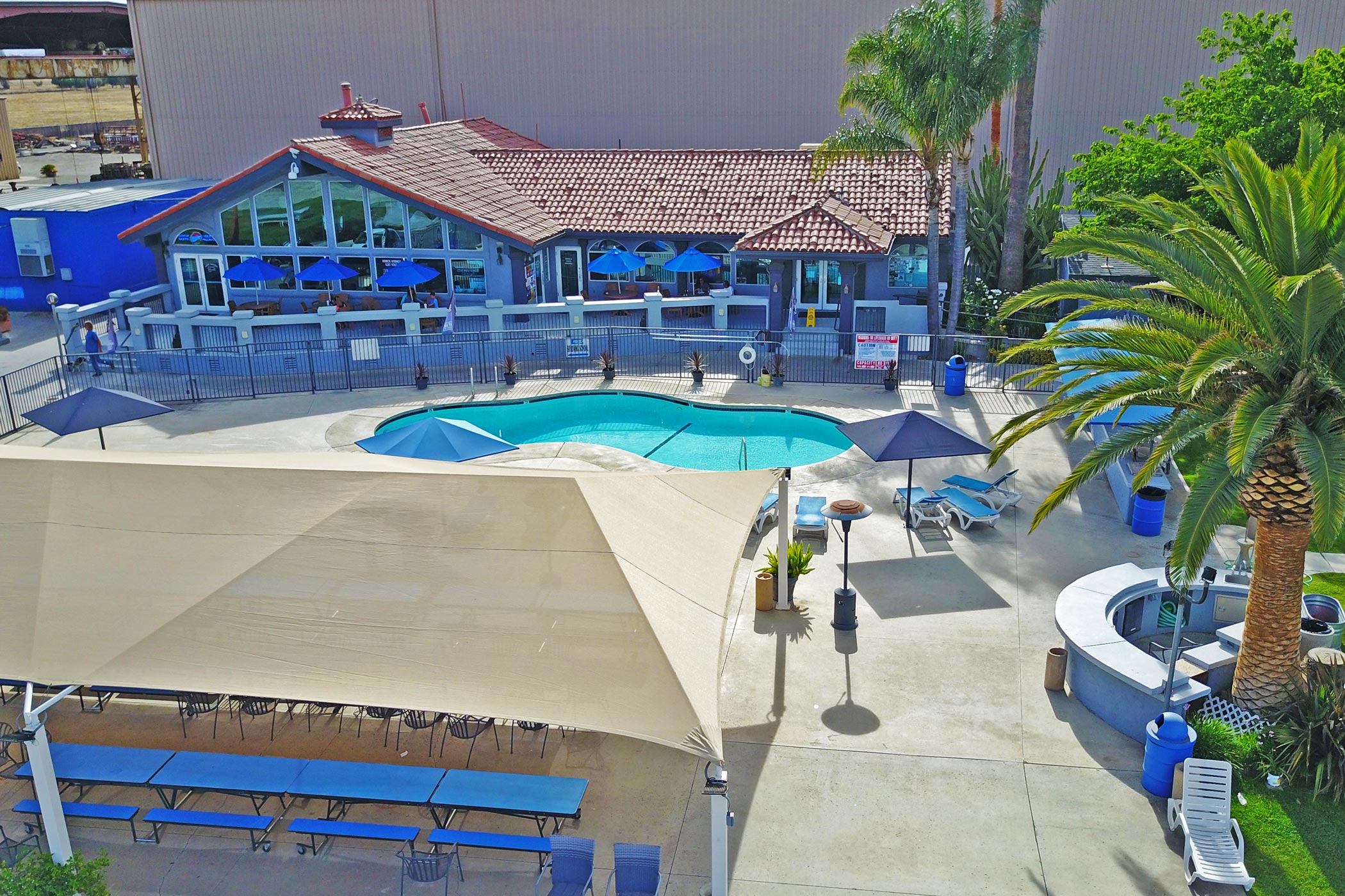 Concrete surrounds a light blue pool in front of a blue building with terra cotta tiles on the roof