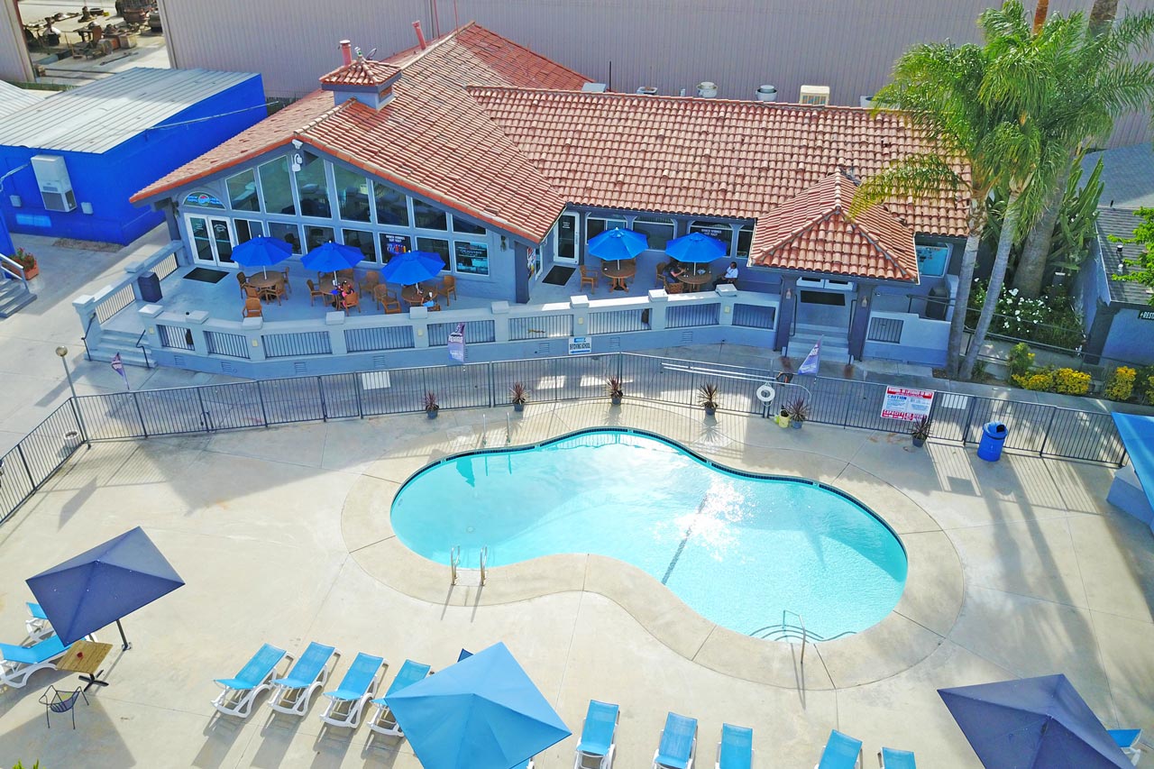 Concrete surrounds a light blue pool in front of a blue building with terra cotta tiles on the roof