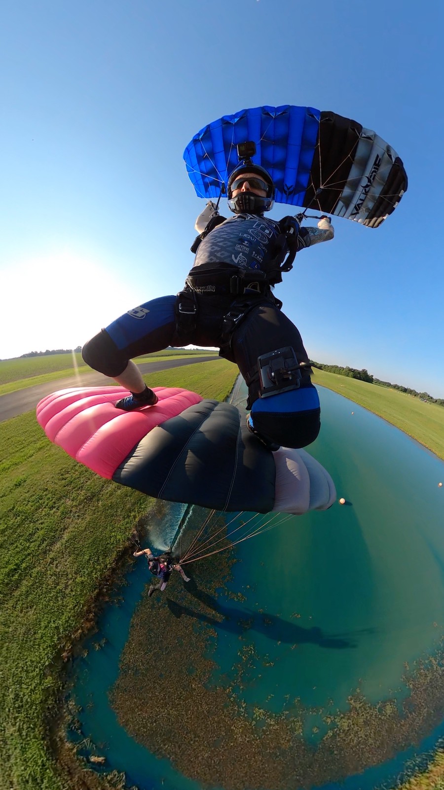 Licensed skydiver with a blue and gray parachute under canopy above a skydiver with a pink and black canopy
