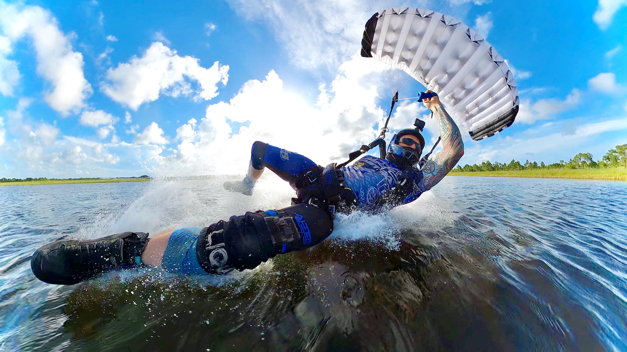 Licensed skydiver in a blue and black jumpsuit skimming the water on landing