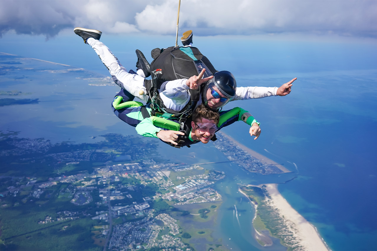 Tandem skydiving student and instructor smiling while in freefall over a beautiful coastline
