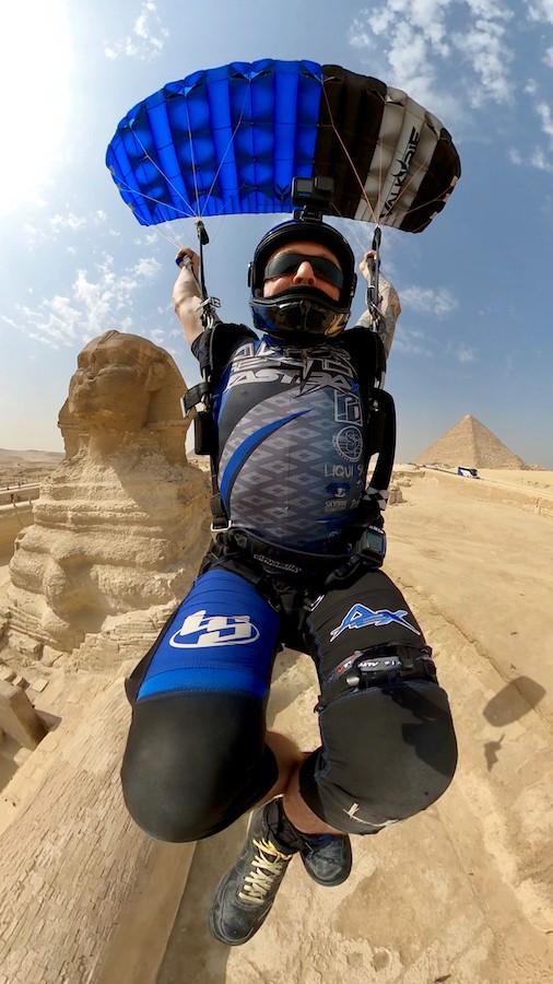 Licensed skydiver in blue and black jump suit and parachute flies canopy in front of the sphynx and pyramids