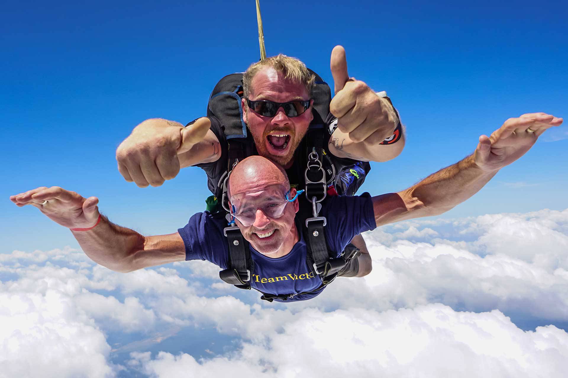 Male tandem skydiving student and instructor in freefall with blue sky and clouds